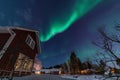 Fantastic winter landscape with wooden house with light in window in snowy mountains and Northern light in night sky. Christmas Royalty Free Stock Photo