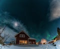 Fantastic winter landscape with wooden house with light in window in snowy mountains and Northern light in night sky. Christmas Royalty Free Stock Photo