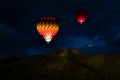 Colorful glowing hot air balloons floating in a night sky over forested mountain peaks Royalty Free Stock Photo