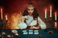 Fantasy beautiful magnificent girl in image of a gypsy sits at table in dark gothic room. Red costume, vintage clothing