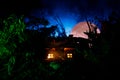 Fantasy decorated photo. Small beautiful house in grass with light. Old house in forest at night with moon. Selective focus Royalty Free Stock Photo