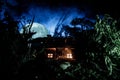 Fantasy decorated photo. Small beautiful house in grass with light. Old house in forest at night with moon. Selective focus Royalty Free Stock Photo