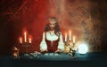 Fantasy girl in image of gypsy witch sits at table in dark gothic room. Art Red costume. Fortune teller magical woman Royalty Free Stock Photo