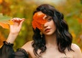 Fantasy girl princess holds red orange autumn fallen maple leaf in hands hides smiling happy face. Sexy woman queen Royalty Free Stock Photo