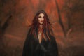 fantasy gothic woman dark witch. Red-haired evil Girl demon in black dress cape hood. Long hair flutters fly in wind