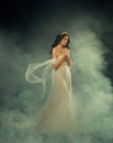 Fantasy Greek goddess woman fashion model walks in dark sky clouds. Girl Aphrodite sexy queen old style myth. White