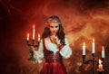 Fantasy gypsy woman in red vintage dress. Long black hair, gold jewelry. Girl witch fortune teller holds a candlestick Royalty Free Stock Photo