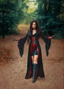 Fantasy halloween woman witch walks in summer nature green forest trees. Gothic girl sexy face, black red dress creative Royalty Free Stock Photo