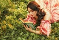 Fantasy happy woman lies on green grass of forest lawn holds in hands magic book novel old style, bright magical sun Royalty Free Stock Photo