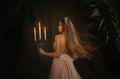 Fantasy medieval girl princess walks in dark gothic room. Woman queen is holding candlestick with burning candles in