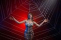 Fantasy photo of spider-queen woman in shiny silver dress, touching large cobweb with hands. Carnival costume black