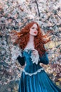 Fantasy portrait red-haired girl romantic princess stands in spring flowering garden. Blooming green tree flowers. Long Royalty Free Stock Photo