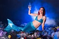 Fantasy stupid mermaid in deep ocean. Plastic water bottles and bags pollution on sea floor. Environmental problem.