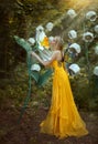 Fantasy woman blonde forest fairy. Fashion model in a long yellow dress with butterfly wings holds in hand and smell