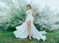 Fantasy woman in long white elegant fashion long dress walks in green spring blossom cherry garden. Happy cheerful girl
