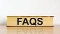 FAQS, frequently asked questions symbol. Book with word `FAQS, frequently asked questions` on beautiful wooden table, white
