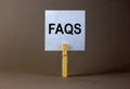 FAQS, frequently asked questions symbol. White paper on wooden clothespin. Words `FAQS, frequently asked questions`. Beautiful