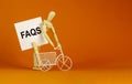 FAQS, frequently asked questions symbol. White paper. Words `FAQS, frequently asked questions`. Miniature bicycle, wooden human. Royalty Free Stock Photo