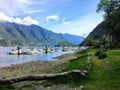 A faraway view from the shore of a beautiful marina full of boats and old inn, surrounded by forest and mountains