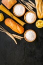 Farinaceous food. Fresh bread and raw pasta near flour in bowl and wheat ears on black background top view copy space Royalty Free Stock Photo