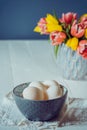 Farm Fresh white eggs in ceramic grey bowl on vintage napkin and vase with fresh pink and yellow tulips on the white wooden table Royalty Free Stock Photo