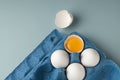 Farm natural products. Fresh white chicken eggs in eco-packaging on a blue background. Broken egg with yolk in the shell. Top view Royalty Free Stock Photo