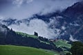 Farm and pine forest in the Austrian Alps with dark dramatic clouds over a steep wooded ridge in the background