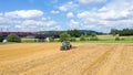 A farm tractor cultivating a harvested field against  a blue sky with clouds Royalty Free Stock Photo