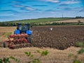 A farm tractor ploughing a field of stubble on a partly sunny day in Autumn. Royalty Free Stock Photo