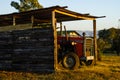 A farm tractor sitting under cover in the early sunshine.