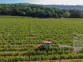 Farm tractor spraying pesticides & insecticides herbicides over green vineyard field