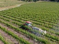 Farm tractor spraying pesticides & insecticides herbicides over green vineyard field