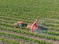 Farm tractor spraying pesticides & insecticides herbicides over green vineyard field
