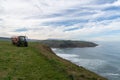 Farm tractor and trailer in a green field next to steep cliffs and ocean on the Spanish coast