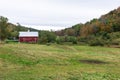 Red barn and grassy field at the foot of wooded hills on a cloudy autumn day Royalty Free Stock Photo