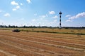 Farm view with a lighthouse and reaped field, windmills on the horizon