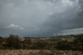 Farm of wind turbines for renewable wind energy on far horizon on hills of Romania under the dark cloudy sky. Copy space Royalty Free Stock Photo