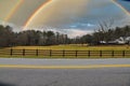 a farm with yellow and green grass surrounded by a street with a yellow line, a black wooden fence and lush green Royalty Free Stock Photo