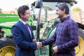Farmer And Businessman Shaking Hands With Tractor In Background Royalty Free Stock Photo