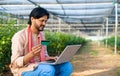 farmer busy making online payment using credit card on laptop while sitting at greenhouse - concept of secure online