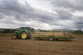 A farmer carries empty wooden bins for potatoes on a trailer towed behind a John Deere tractor across a farm field Royalty Free Stock Photo