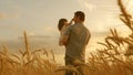 Farmer carries a little daughter in his arms through a field of wheat. happy child and father are playing in field of Royalty Free Stock Photo