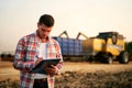 Farmer controls loading wheat from harvester to grain truck. Driver holding clipboard, keeping notes, cargo counting