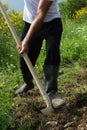 Farmer digging the soil with the shovel, young adult man with rubber boots