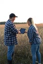 The farmer explains to the woman and shows the yield indicators of wheat fields on the tablet. Standing in a field of Royalty Free Stock Photo