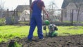 A farmer in the garden tills the land with a motorized cultivator or power tiller, preparing the soil for planting crops