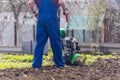 A farmer in the garden tills the land with a motorized cultivator or power tiller, preparing the soil for planting crops Royalty Free Stock Photo