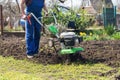 A farmer in the garden tills the land with a motorized cultivator or power tiller, preparing the soil for planting crops Royalty Free Stock Photo