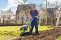 A farmer in the garden tills the land with a motorized cultivator or power tiller, preparing the soil for planting crops Royalty Free Stock Photo