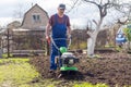 A farmer in the garden tills the land with a motorized cultivator or power tiller, preparing the soil for planting crops Royalty Free Stock Photo